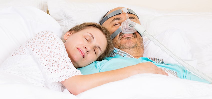 Man sleeping in bed with partner while undergoing CPAP therapy